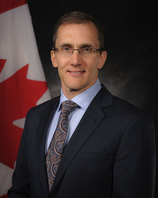 a person in a suit and tie standing in front of a canadian flag