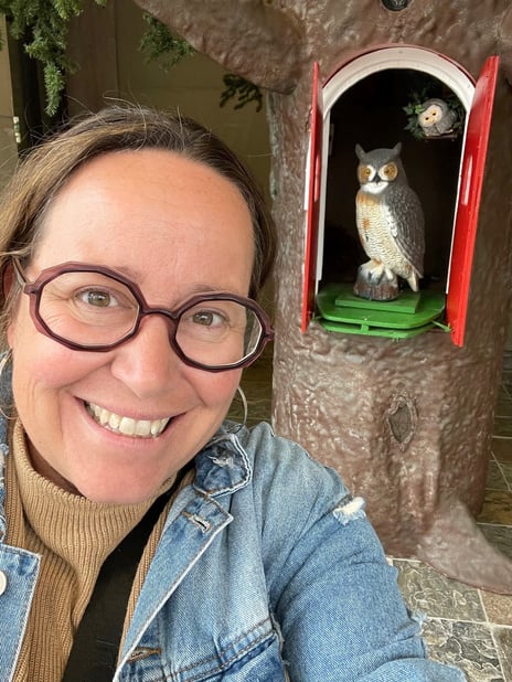 a person wearing glasses and a jacket is taking a selfie in front of an owl